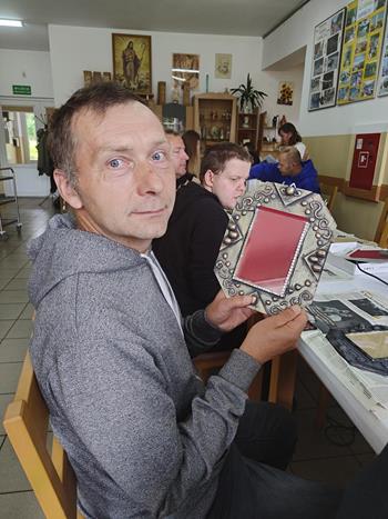 Uczestnik w szarej bluzie prezentujący wykonaną własnoręcznie ramkę na zdjęcia